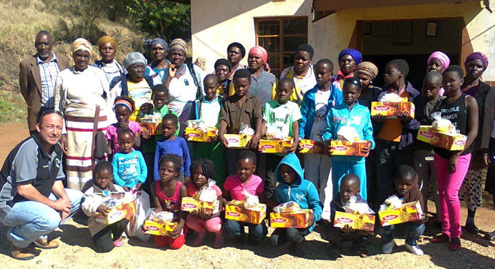 A diverse group of children and adults joyfully holding boxes of food, showcasing community support and togetherness.