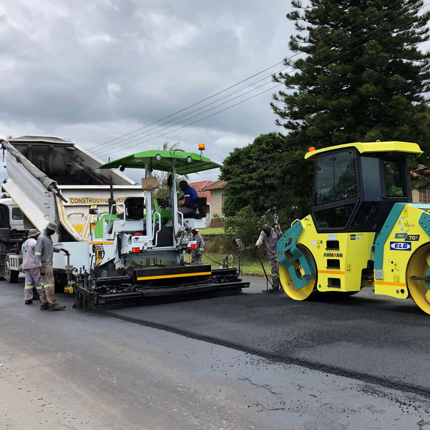 A man operates a roller on a road, compacting the surface for improved durability and safety.