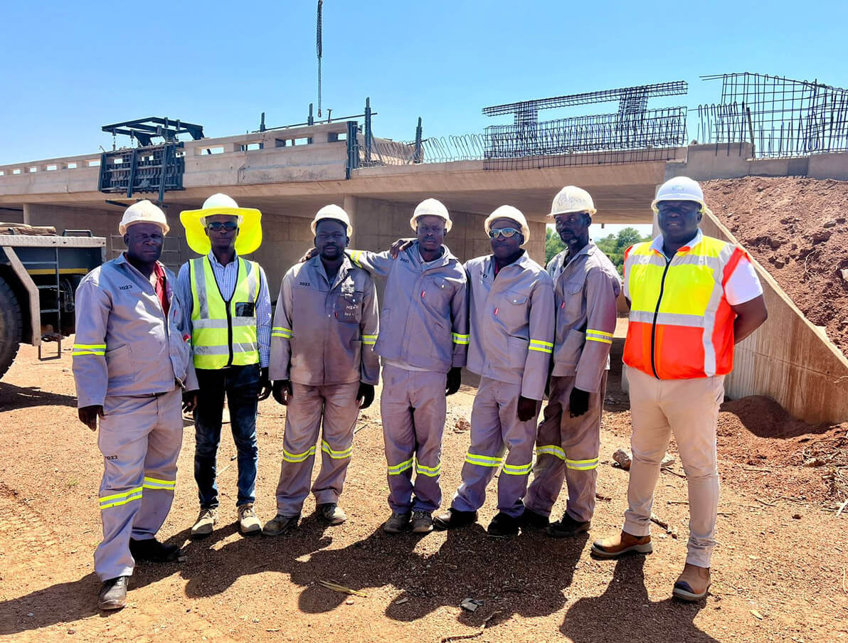 A group of men wearing hard hats stands beside a construction site, discussing plans and overseeing the ongoing work.