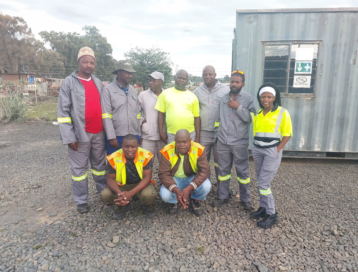 A group of men in work attire standing together, smiling for a photograph in a professional setting.